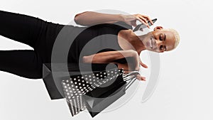 Black Friday shopping, smiling black woman holding many shopping bags and talking at cell phone, isolated on background in various