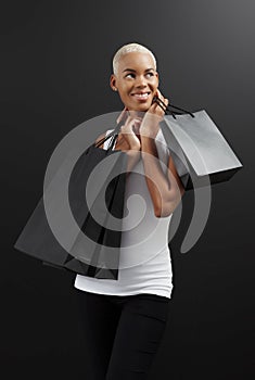 Black Friday shopping, a stunning smiling black woman holding many black bags, against a black background, look to the side, happy