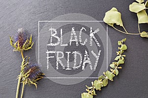 Black friday word written in white chalk on black stone with flower and leaves