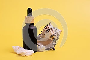 Black frosted glass bottle with a pipette with shells on an isolated yellow background.