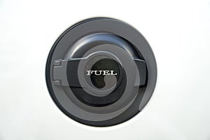 Black fuel filler door with lettering FUEL on a white car.
