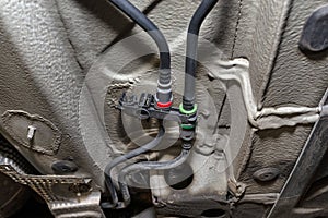 Black fuel lines mounted under the cars chassis, view from the bottom of the car on a jack in a car workshop.