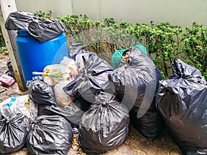 Black garbage bag pile near municipal trash bin full on sidewalk