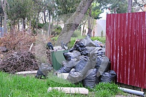 Black garbage bags near the fence of private house and an overturned trash can.