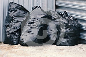 Black garbage plastic bags stand near a metal fence. Waste disposal or landfill site.