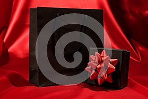 Black gift box with black shopping bag on red fabric