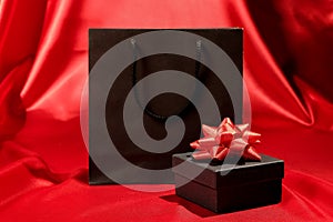 Black gift box with black shopping bag on red fabric