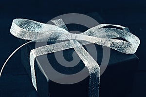 Black gift box with silver ribbon bow on black background. Tonned photo.