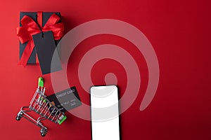 Black gift and red ribbon with black tag on red color background, Black credit card inside small cart and smartphone for shopping.