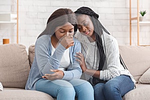 Black girl embracing and comforting her upset friend at home