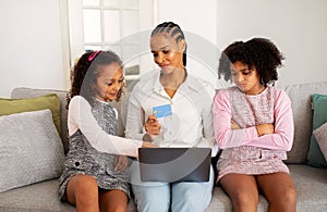 Black Girl Envying Shopping Online With Mother And Sister Indoor