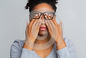 Black girl in glasses rubs eyes, suffering from tired eyes