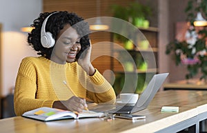 Black girl in headphones studying online, using laptop at cafe