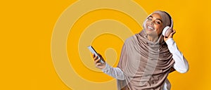 Black girl in headscarf and wireless headphones listening music on smartphone