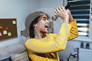 Black girl holding microphon singing karaoke at home, recording songs for contest