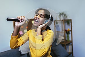 Black girl holding microphon singing karaoke at home, recording songs for contest