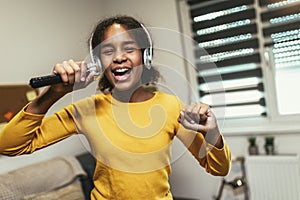 Black girl holding microphon singing karaoke at home, recording songs for contest. Children's lifestyle concept