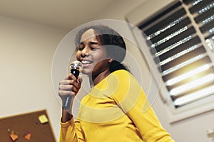 Black girl holding a microphone singing karaoke at home, recording songs for a contest. Children's lifestyle concept