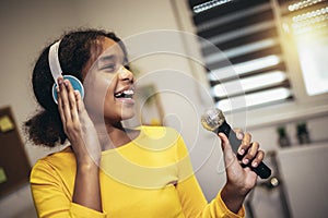 Black girl holding a microphone singing karaoke at home, recording songs for a contest. Children's lifestyle concept