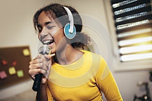 Black girl holding a microphone singing karaoke at home, recording songs for a contest. Children's lifestyle concept