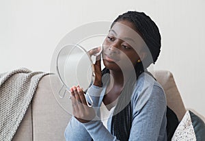 Black girl looking to mirror and cleaning face with cotton pad