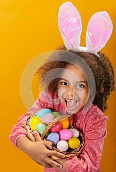 A Black girl with rabbit ears on her head with a basket full of colored eggs.