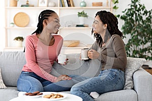 Black girlfriends enjoying weekend together, drinking coffee on couch