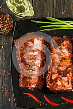 A black glass plate of juicy smoked spareribs with red peppers,