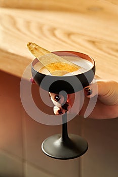 Black glass of spicy cocktail with caramelized pear in female hand photo