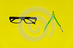 Black glasses and colorful green compasess for circle drawing in school or education colorful yellow background