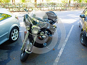 Black glossy motorcycle parked on the roadside between cars on a spring day