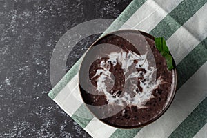 Black Glutinous Rice Porridge or Bubur Pulut Hitam in Malay with coconut milk on dark background on top napkin