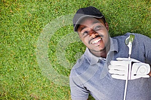 Black golfers put on white gloves and putting the golf clubs on chest while lying on the green grass