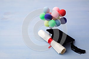 Black Graduation Cap, Degree and balloons on light blue Wooden Background.