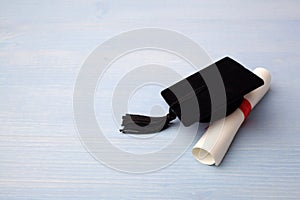 Black Graduation Cap with Degree on light blue Wooden Background.