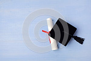 Black Graduation Cap with Degree on light blue Wooden Background.