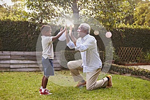 Black grandfather plays with grandson in garden, full length