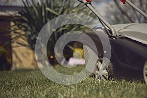 Black and gray modern grass-cutter mowing green lawn in a garden of country house. Gardening care equipment. Close up