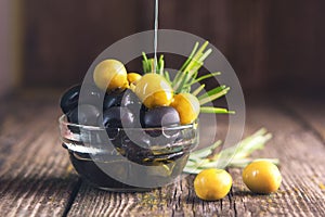 Black and green olives mixed in the bowl on wooden table. Olive oil pouring from olive