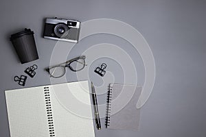 A black and grey working items with notebook, coffee cup, glasses and pen on the gray background.