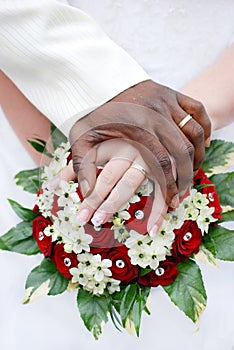 Black groom and white fiance hands on bouquet