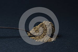 Black ground pepper on a black background. A spoonful of ground black pepper.