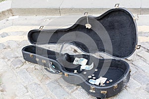 Black guitar case placed on the floor with coins and bills, a payment tip to a street performer