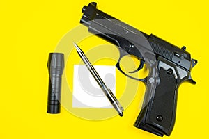 Black gun, reminder note paper, pen and flashlight lies on a yellow background. Private detectives work. Searching information