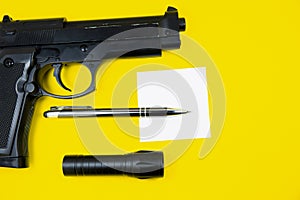 Black gun, reminder note paper, pen and flashlight lies on a yellow background. Private detectives work. Searching information