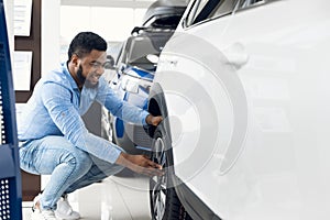 Black Guy Checking Car Wheels And Tyres In Dealership Showroom