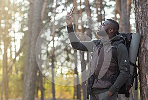 Black guy holding smartphone up, looking for gps in woods