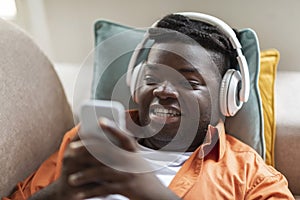 Black guy lying on couch with phone and headphones