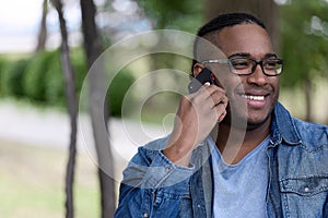 Black guy with a phone walks alone in the park in clear sunny weather