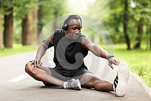 Black guy sportsman sitting on park path, stretching